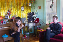 Load image into Gallery viewer, Band members in a cozy living room with vintage decor, gold fringe backdrop, and eclectic furnishings.