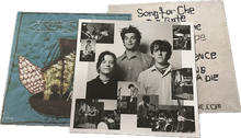 Load image into Gallery viewer, A music album package shown at an angle, featuring a collage of black-and-white band photos on an inner sleeve, a blue embroidered front cover, and a beige fabric design on the back cover
