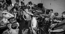 Load image into Gallery viewer, Band performing on stage with an audience in a dark venue
